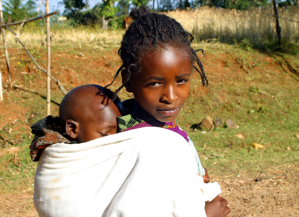 A young girl child in Zambia carrying her younger sibling on her back.